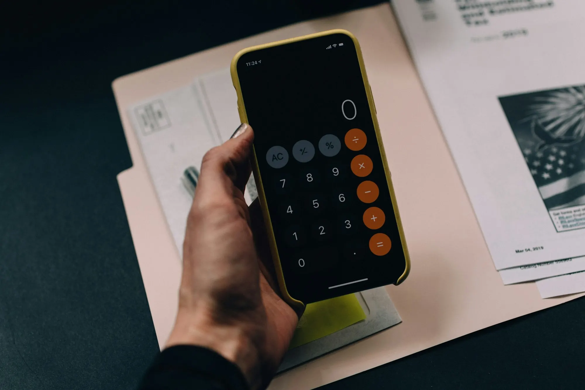 Calculator resting on a stack of mortgage and closing documents while a homebuyer totals up costs