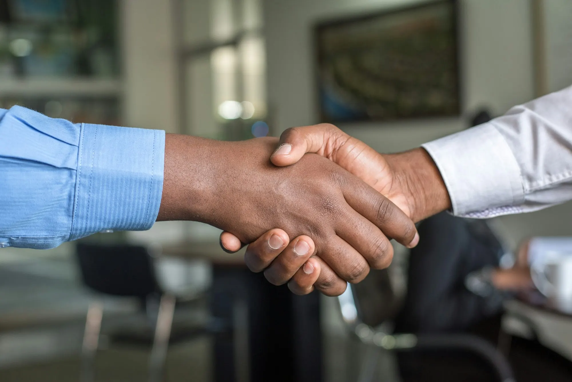 Real estate agent and client shaking hands across a table after agreeing representation terms