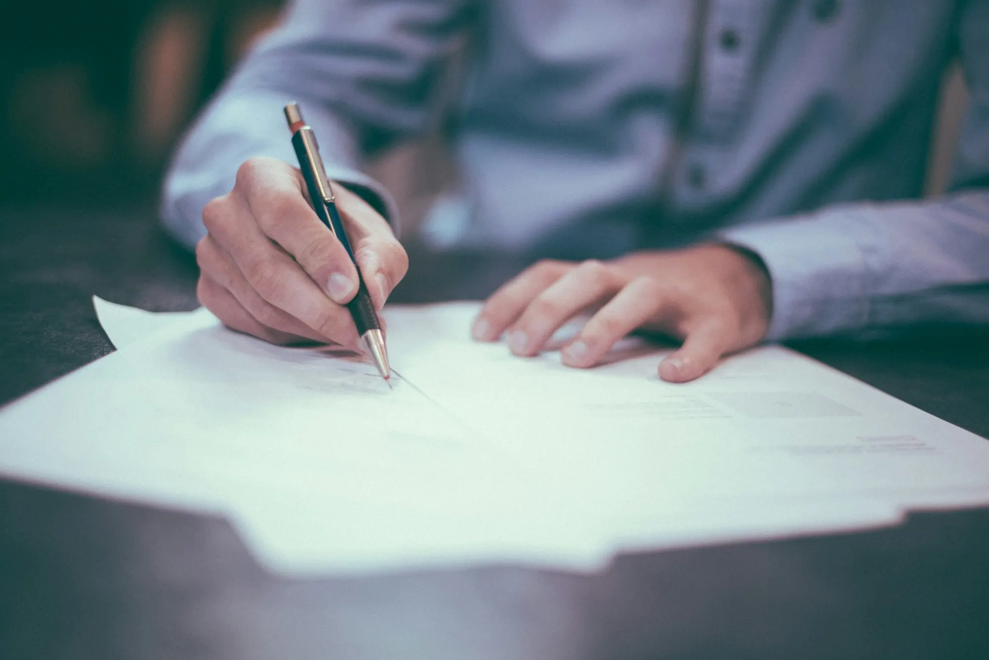 Homebuyer signing a real estate purchase contract with a pencil at a desk