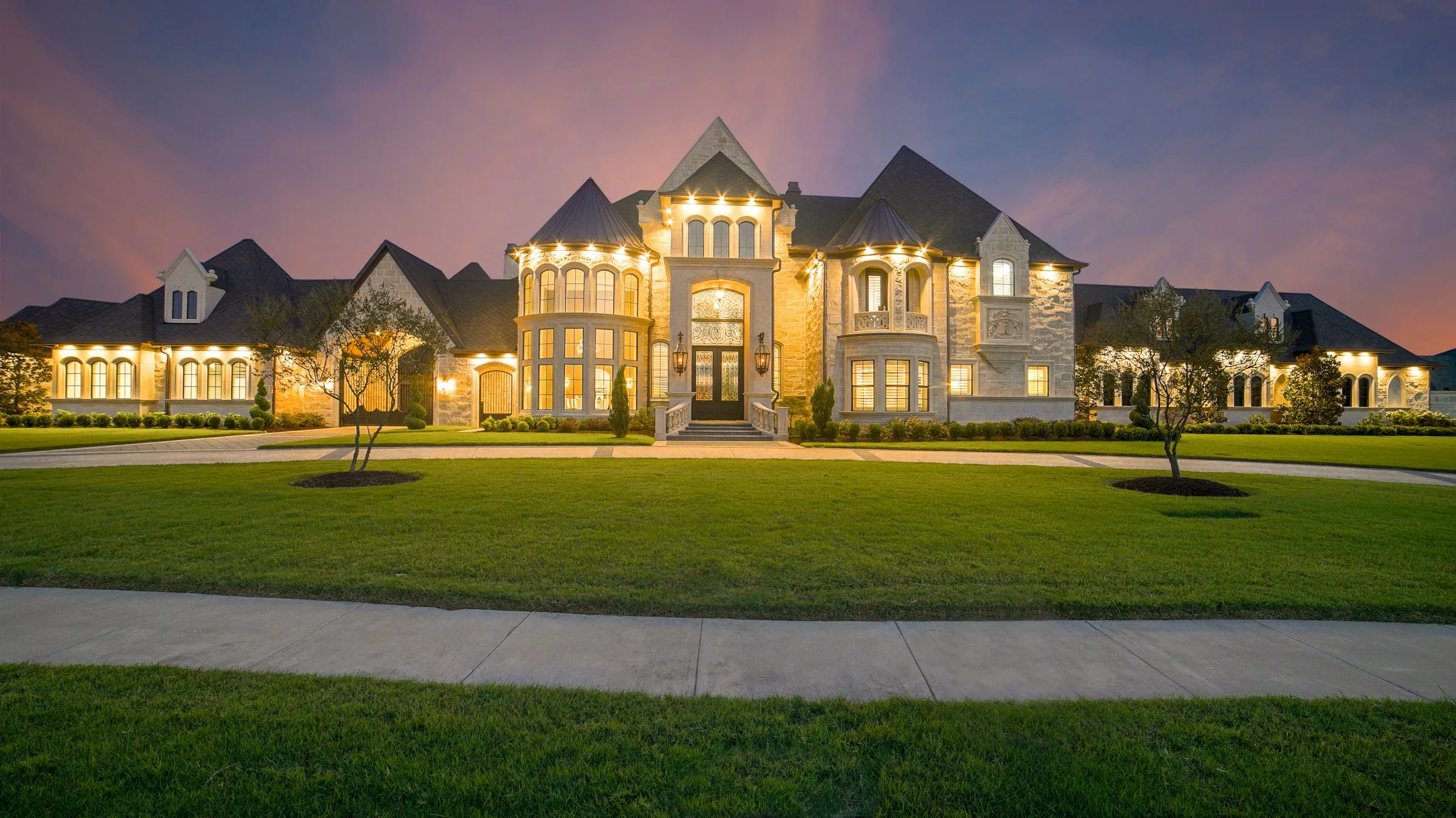 Modern luxury American home exterior at dusk with warm interior lighting glowing through floor-to-ceiling windows